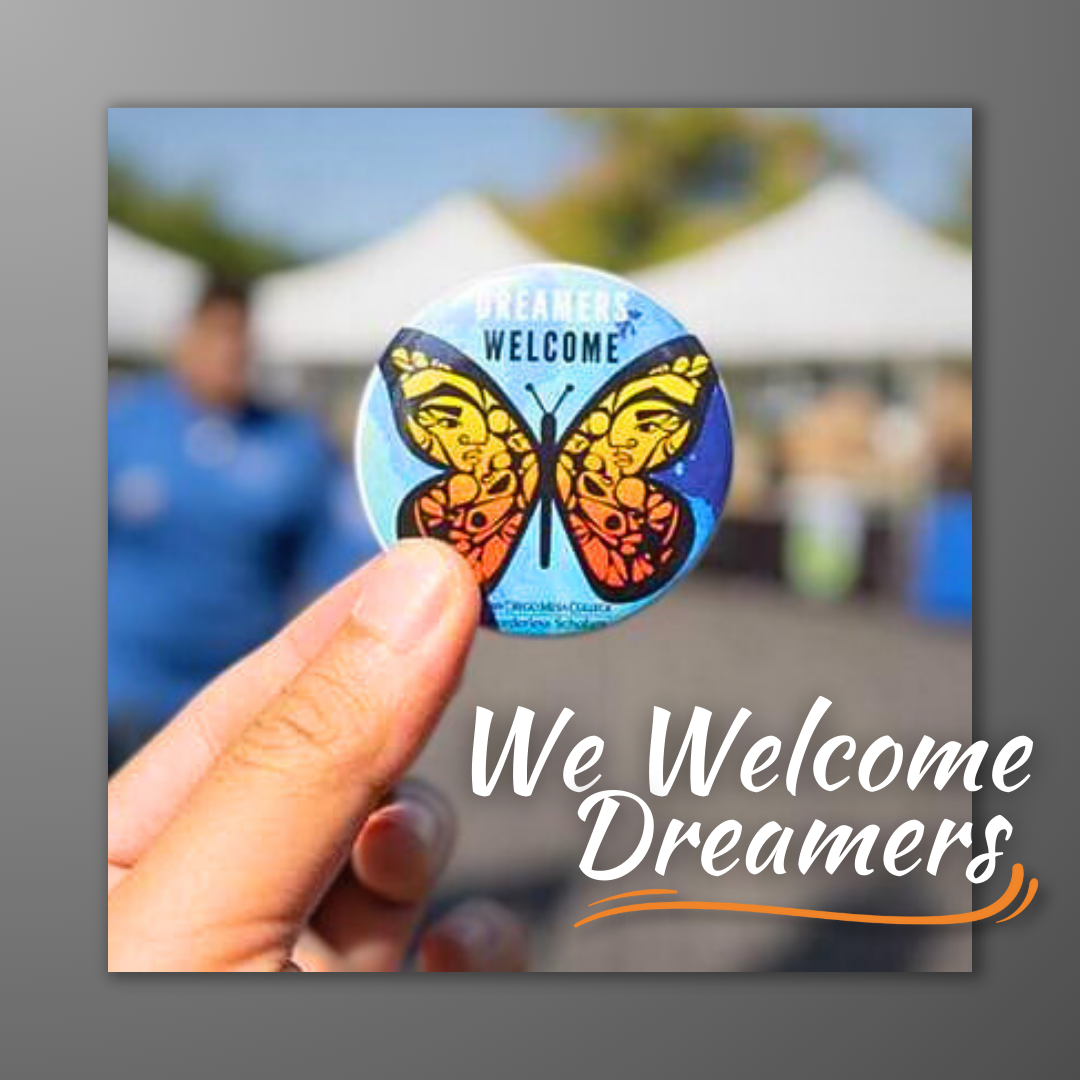 A closeup image of a hand holding up a butterfly button-pin. Image text: We welcome Dreamers.