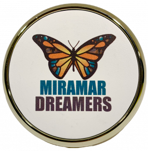 A photo of a chrome and leather drink coaster with the Miramar Dreamers butterfly logo printed on it.
